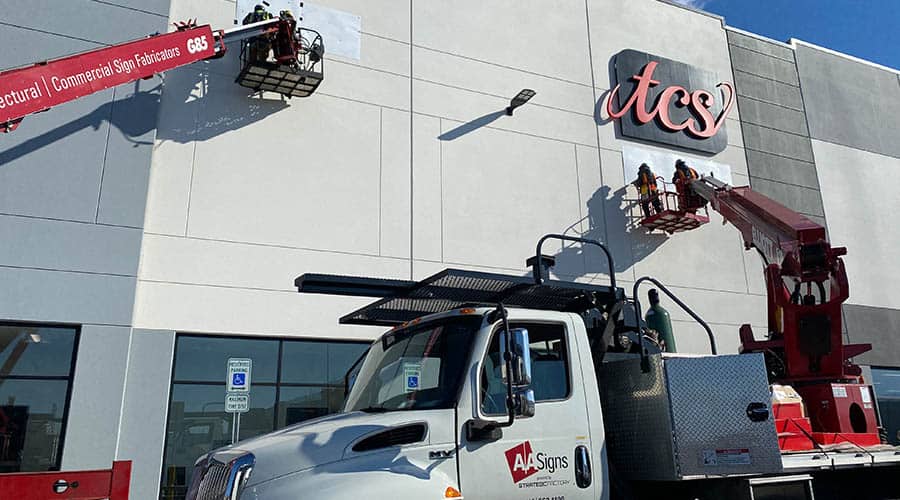 signage crew installing building signage using trucks and lift equipment